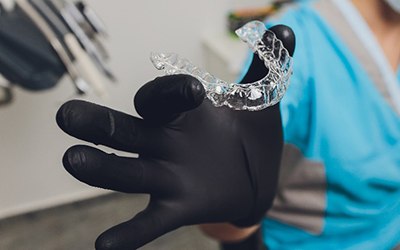 Dentist holding Invisalign clear aligner with black glove