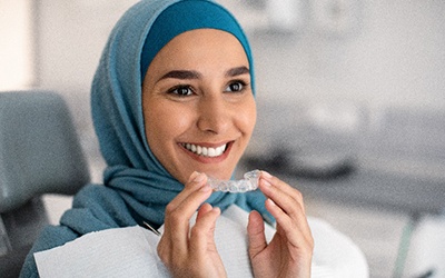 Closeup of woman smiling while holding clear aligner in treatment chair