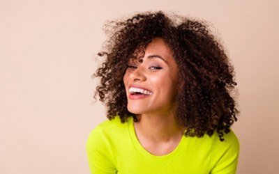 Woman in neon green shirt and curly hair smiling with veneers