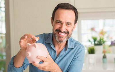 Smiling man putting money in a piggy bank