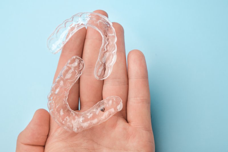 Two clear aligners resting on a hand in front of blue background