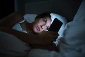 Woman lying in bed looking at cell phone
