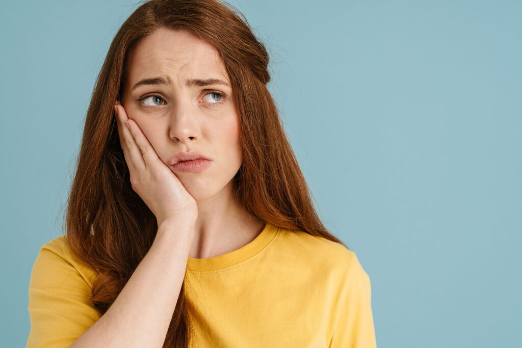 Woman in yellow shirt holding her hand to her sore jaw